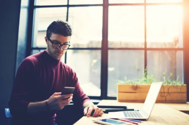 Gün ışığı alan dizüstü bilgisayar ile coworking ve ücretsiz 4 g internet bağlantısı kullanarak otururken bildirim smartphone cep telefonu ile okuma gözlük erkek öğrenci. Erkek üzerinde cep SMS mesajı gönderme