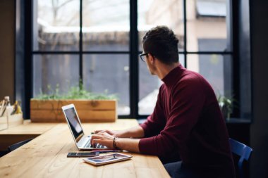 Metin tipik dizüstü bilgisayar klavye üzerinde pencereden dışarı bakarken yaratıcı erkek grafik tasarımcı. Sohbet Online ile sokulgan yolu ile yüksek hızlı internet bağlantısı coworking içinde oturan öğrenci