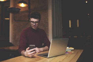 Emin iyi görünümlü grafik tasarımcı bildirim internet'e bağlı ve sosyal ağlarda Studio otururken takipçileri ile sohbet smartphone cep telefonu ile kontrol gündelik kıyafeti giymiş