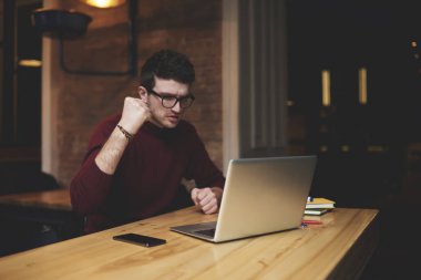 Yakışıklı deneyimli tüccar duygusal mali alışverişi zaferini kutluyor trendy giyim giymiş. Genç hipster adam gözlük dikkatlice dizüstü bilgisayar başında oturma kapalı iken arıyorsunuz