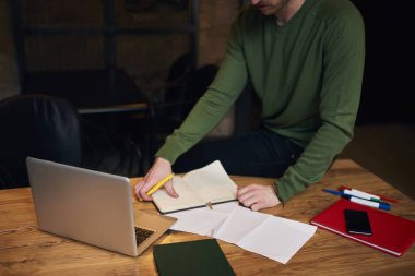 Kırpılmış görüntü yaratıcı erkek öğrenci dizüstü bilgisayar kullanan yaklaşan sınavına hazırlanması için wifi bağlıyken tahta masada oturan ve Bilişim analiz trendy kıyafeti giymiş