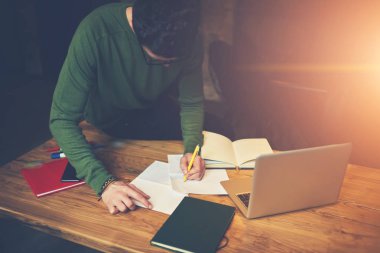 Yetenekli erkek öğrenci ders kitabı seminer için hazırlanırken bilgileri yazma yeşil Kazak giymiş. Dikkatli planlama çalışma süreci güneş stüdyoda oturan başarılı girişimci
