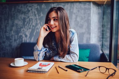 Profesyonel tasarımcı modern smartphone arkadaşı ile defter ve lezzetli kahve kapalı tahta masada oturan moda giyim yeni skeçler üzerinde çalışırken konuşmak gülümseyen