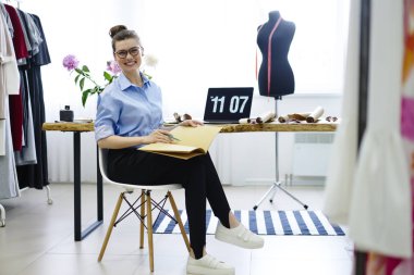 Portre profesyonel terzi moda sanayi olay planlama hazırlanması kameraya bakarak gülen neşeli genç Yöneticisi çalışma programı çalışma tablosunda oturan showroom, düzenleme 