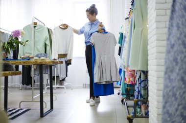 Genç kadın tasarımcı seçimi kendi yeni koleksiyon ayakta için showroom elinde renkli elbiseler Giydir. Moda stilist geliştirme iş için son moda tekstil üretimi ile çalışma