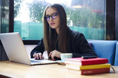 Dizüstü bilgisayar aygıt ve kitaplar kameraya bakarak ve kahvehane iç wifi bölgesinde oturan yaklaşan sınavlar için hazırlanıyor süre oturan güzel akıllı öğrenci portresi yarım uzunluk