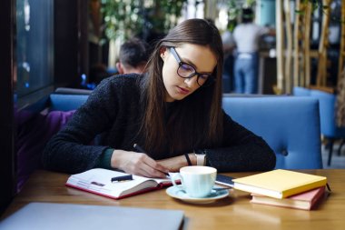 Dalgın esmer kadın Tasarımcısı oturan kafede kahve molası, rapor için accountings dikkat çeken ev ödevi görev yapmayı durulması Eyewear zeki öğrenci not defterindeki kroki çizim konsantre