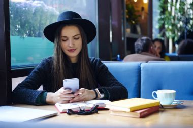 Trendy şapka olarak sosyal ağlar ile sokulgan yolu ile birlikte oturan cep sohbet online içinde şık genç kadın kahve dükkanında kitap. Erkek kafede okurken cep telefonuna SMS mesajı okuma