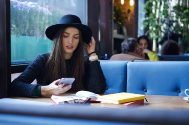 Profil sosyal ağlar mesajları ve bildirimler mobil, çekici şık giyimli blogger takipçileri kafede smartphone üzerinden sohbet üzerinde okuma kontrol şapkalı büyüleyici hippi kız