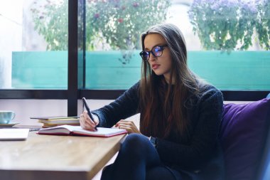 Dalgın esmer tasarımcı not defterinde kafede oturmuş, zeki kız öğrenci Eyewear çizerken oluşturma kroki üzerinde durulması rapor için bilgi analiz ödev yapmaya konsantre