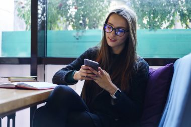 Pozitif hippi kız şık gözlükler arkadaş manifatura iletileri smartphone cep telefonu ile sohbet keyfi içinde wifi için bağlı. E-posta kutusu hakkında geribildirim alma kafede oturan çekici genç kadın