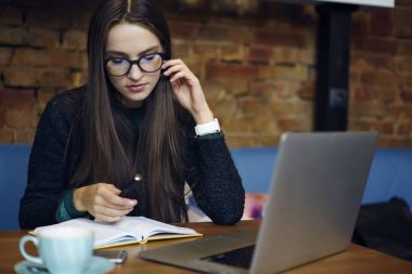 Kahve dükkanında öğrenme günlüğü fikir belirterek eğitim görev için planı yapma bardaklarda dalgın genç öğrenci. Tarama için dizüstü bilgisayar kullanarak proje oluşturma sırasında durulması kafede çalışan yetenekli tasarımcı