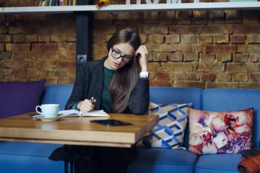 Şık gözlükler kafede kahve molası sırasında proje planlama düşünceli genç iş kadını. Mali rapor yazma Not Defteri'nde yapma accountings konsantre ciddi kadın girişimci