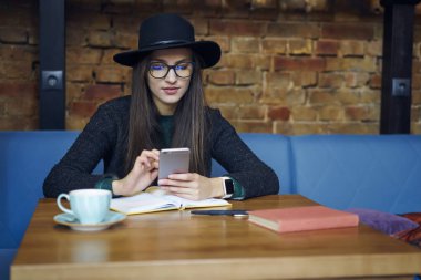 Çekici kız öğrenci kafe iç sohbet arkadaşlar sosyal ağlar, güzel hippi kız blogging tatilinde Wi-Fi bağlantısı kullanarak smartphone üzerinden ücretsiz vakit trendy şapkalı