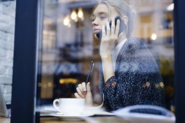 Ciddi sarışın Yöneticisi penceresi ekran iş hakkında konuşmayı yakınındaki kafede oturan planları, rahat kıyafet cep telefonunuzda meslektaşı ile konuşurken kafede oturan genç kız öğrenci