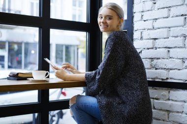 Satınalmalarda, neşeli blogger payı multimedya dosyalarını dijital tablet ve wifi kullanarak Web sitesinde alışveriş yapma kafede oturan sarışın kadın hippi kız gülümseyerek portresi memnun
