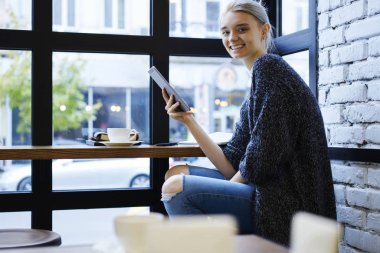 Neşeli sarışın hippi kız memnun kullanma online alışveriş yapma web mağaza satın almalarla touchpad ve wifi bağlantı kafe, yaratıcı blogger takipçileri ile sohbet gülümseyen portresi