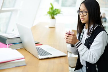 Sıcak içecek, alan coworking içinde serbest zaman sırasında eğitim webinar üzerinden bilgi öğrenmek için dizüstü bilgisayar kullanan öğrenci zevk mola sırasında film izlerken Eyewear genç uluslararası öğrenci