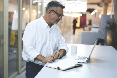 Dizüstü bilgisayarda finans haberleri rapor gelirler, deneyimli girişimci dijital tablet kullanarak pazarlama video izlerken uzaktan işi yaparken okuma profesyonel olgun işadamı