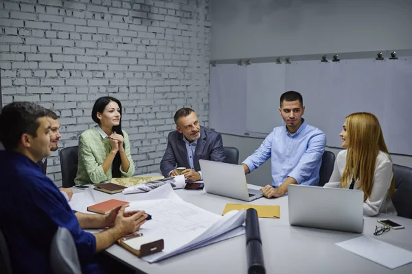 Yeni bina ofiste tabloda toplantı oturan proje oluşturma hakkında fikirleri tartışmak erkek ve dişi profesyonellerinden oluşan grup. Pazarlama uzmanları mimari planlar brifing sırasında analiz