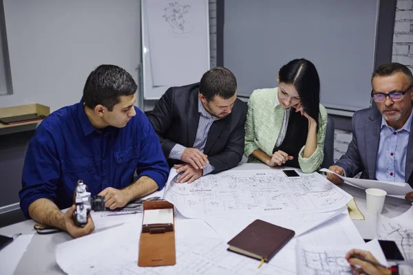 Profesyonel ekibi, deneyimli mühendis ofis iç tabloda toplantıda planlama oturma binanın mimari çizimler üzerinde çalışıyor. erkek ve kadın tasarımcılar planları üzerinde beyin fırtınası sırasında işbirliği