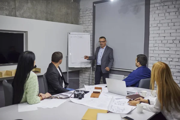 Yetenekli olgun erkek Yöneticisi eğitim çalışanları için yapma ve ana iş kavramları açıklayan formal giyim giyinmiş. Deneyimli CEO'su ofiste iş arkadaşları iş başlangıç projesi ile tartışılması