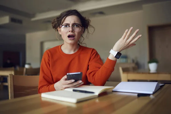 Portrait of confused hipster girl sitting with open mouth disappointed of examination testing receiving feedback on smartphone connected to internet, young student angry about bug in phone application