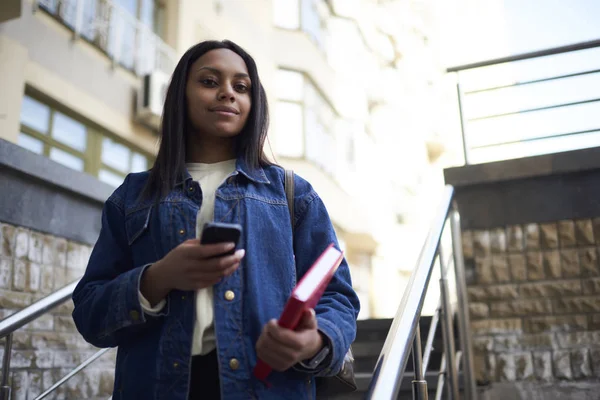 Portre çekici esmer öğrencinin Kot ceket kitapla sokak kontrol e-posta-mobil, smartphone navigasyon kullanarak toplantı için gezinme afro Amerikan hippi kız yürürken
