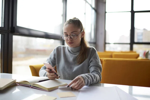 Pensive businesswoman searching information about partners using visit card contacts.Concentrated female manager texting email address of web page from card to making online booking sitting in cafe