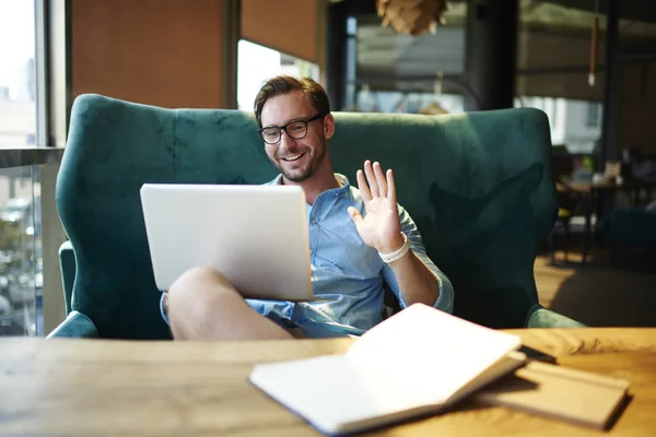 Handsome businessman waving communicating in video chat with colleagues discussing ideas for project in cafe.Cheerful entrepreneur having online conference with client satisfied with friendly tal