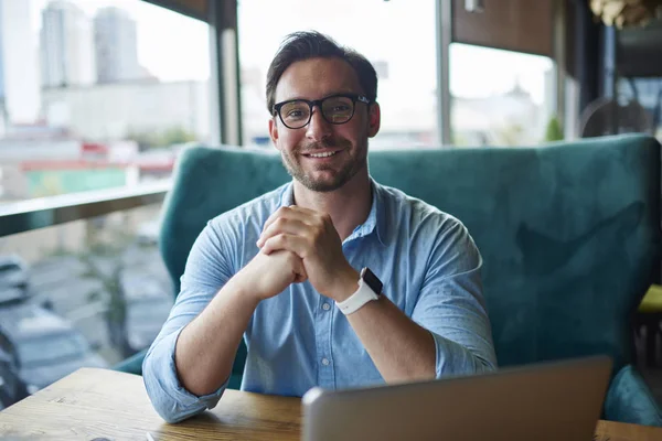 Portrait of handsome freelancer satisfied with completing online project successfully made great work, prosperous businessman in eyewear using laptop computer for distance job sitting in coffee sho
