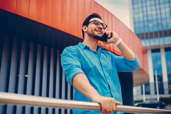 Smiling male traveler happy receiving call in roaming talking about trip while standing outdoors, positive hipster guy talking with best friend ob phone satisfied with good mobile connection