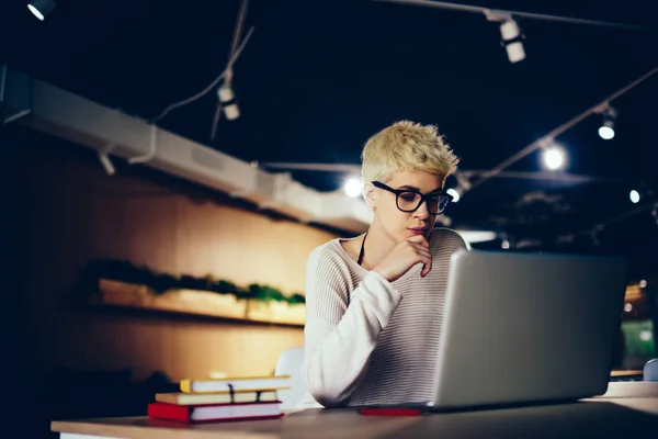 Clever trendy dressed female student working productively on coursework reading information on laptop,skilled creative designer analyzing plan for task pondering on problem solution in loft interior