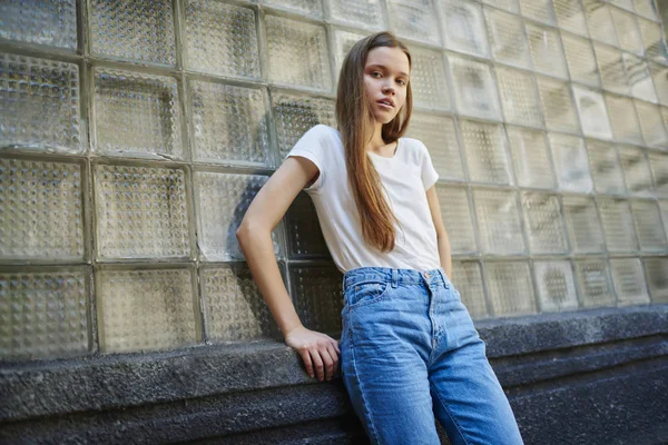Portre çekici genç bayan moda giyim ayakta kentsel cam duvar, beyaz t-shirt markası veya etiket camer için poz için kopyalama alanı alanı ile güzel teen modeli