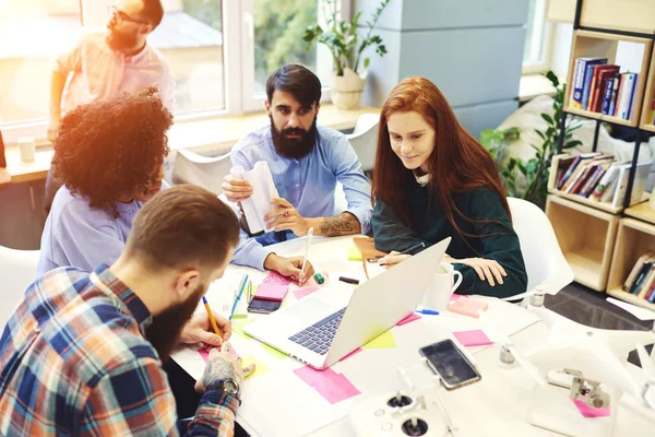 Genç erkek ve dişi Öğrenciler üniversite kitaplığında dizüstü bilgisayar ve Wi-Fi erişimi ile birlikte muayene için hazırlanıyor, yetenekli tasarımcıları yaratıcı proje tartışmak için tablo toplantı sahip planı