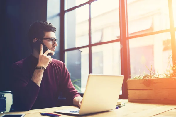 Handsome serious entrepreneur having mobile conversation with colleague on telephone using application and discussing ideas for startup project.Pondering good looking male talking on cellular