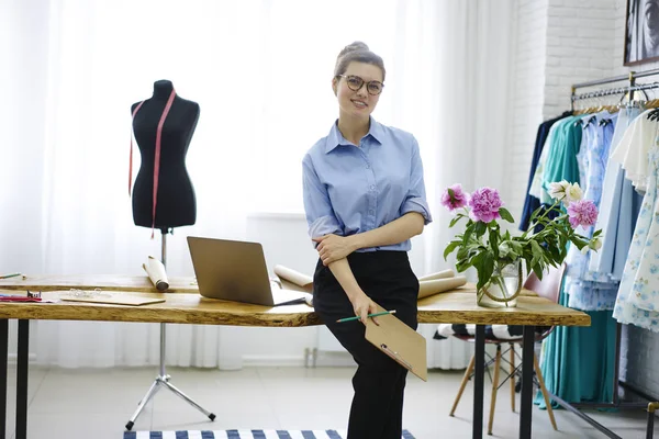 Portrait of attractive female owner of showroom planning event of fashion industry standing near working place,charming trendy dressed creative manager satisfied with occupation making clothes