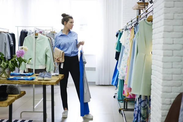 Çekici trendy giyim mağaza seçerken, profesyonel stilist müşteri seçimi tasarımcı dükkanda konsantre trendy görünümünü oluştururken uygun kavram kullanarak kadın müşteri giyinmiş 