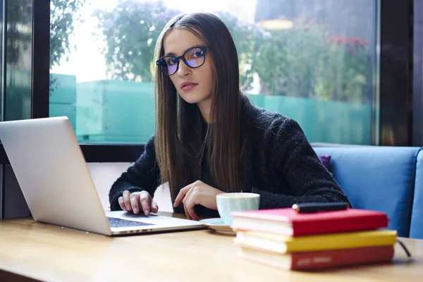 Dizüstü bilgisayar aygıt ve kitaplar kameraya bakarak ve kahvehane iç wifi bölgesinde oturan yaklaşan sınavlar için hazırlanıyor süre oturan güzel akıllı öğrenci portresi yarım uzunluk