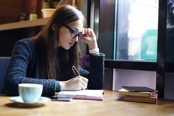 Kafede not defterinde rapor yazma öğrenme Eyewear yetenekli esmer kız öğrenci. Profesyonel grafik tasarımcı taslak oluşturma konusunda durulması kafe iç çalışmalarında konsantre