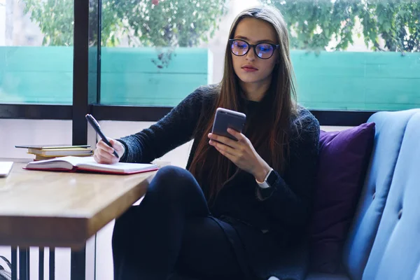 Bilgi günlüğü içinde smartphone ile haberleri okurken dikkat çeken Eyewear dalgın esmer genç kadın. Bilet rezervasyon ve kafede oturan web sayfasında ödeme yapmadan güzel kız öğrenci