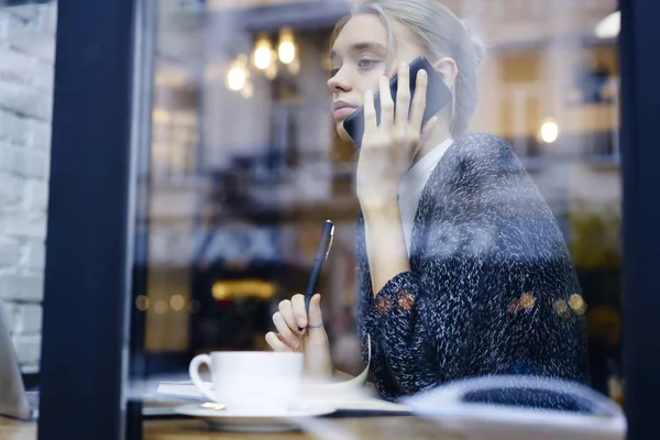 Ciddi sarışın Yöneticisi penceresi ekran iş hakkında konuşmayı yakınındaki kafede oturan planları, rahat kıyafet cep telefonunuzda meslektaşı ile konuşurken kafede oturan genç kız öğrenci
