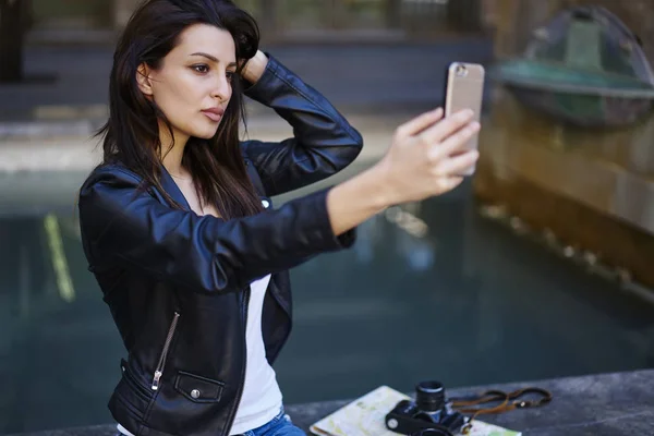 华丽的女性博客在时髦的服装造型 在智能手机相机上拍摄坐在城市设置 黑发的时髦女孩 使自拍在社交网络共享户外休息 — 图库照片