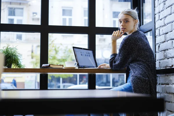 Dizüstü bilgisayar ile sahte kadar uzak iş uygulaması güncelleştiriliyor kafe iç, yetenekli kadın Tasarımcısı ekran üzerinden çalışma görev tamamlama hakkında düşünme dalgın sarışın freelancer portresi