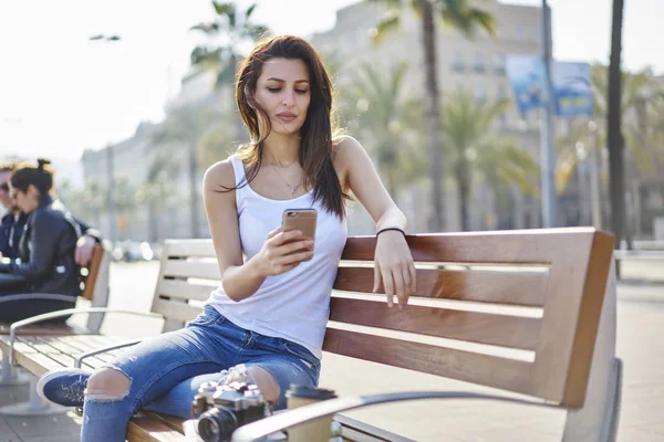 有吸引力的女性游客检查通知在智能手机制作银行业务在线通过4G 连接户外 时髦的女孩坐在长椅上春季晴天博客网络 — 图库照片