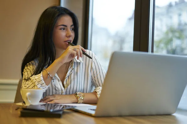 Attractive business woman making creative solutions while working on startup project in cafe, beautiful female entrepreneur pondering on solving problems while updating software on laptop computer