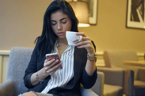 社会チャット香りコーヒーのカップで休んでいる魅力的な女性マネージャー ネットワークのメール 仕事の休憩中にスマート フォンでビデオを見て物思いにふける女性起業家のメッセージの受信 — ストック写真