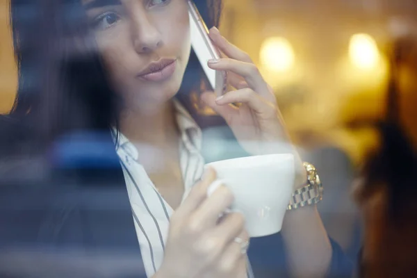 Experienced business woman in elegant wear talking on smartphone with colleague during coffee break, close up of charming brunette entrepreneur having serious mobile conversation about project in cafe