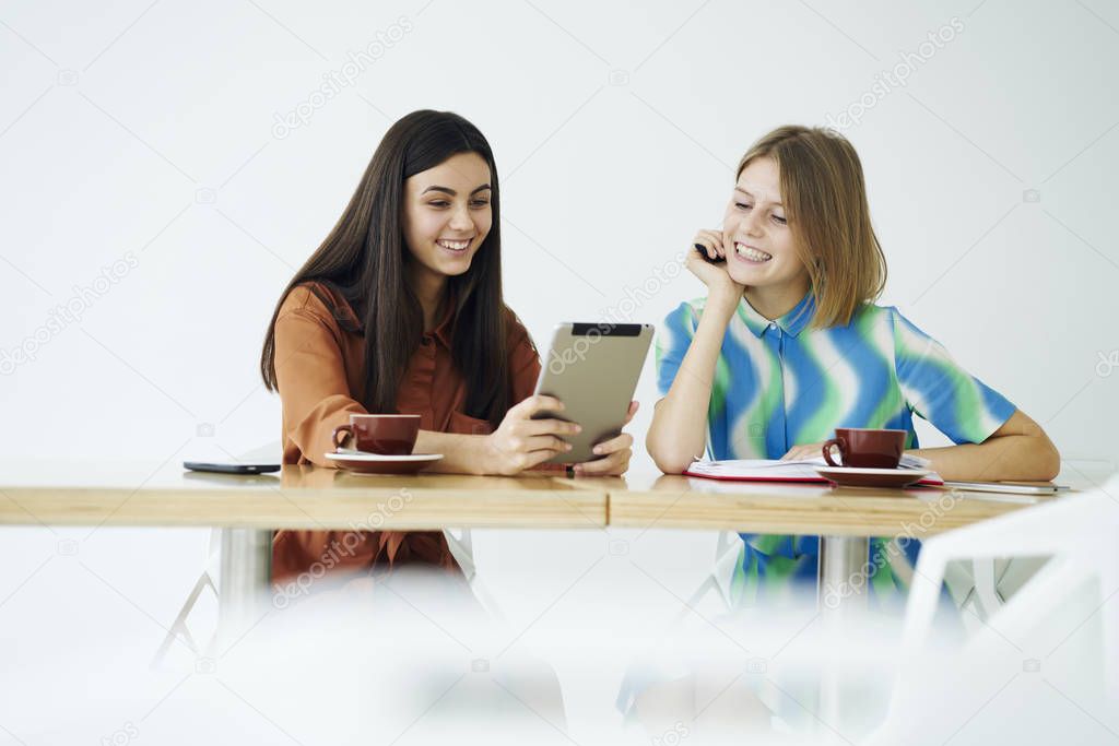 Cheerful young attractive friends enjoying free time together in coffee shop watching funny videos from social networks via digital tablet connected to wifi sitting against copy space for advertising 