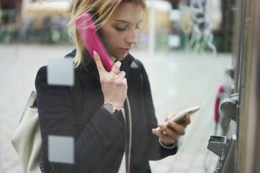 Dalgın genç kadın Gezgin arama numarasına uluslararası kod 4 g bağlantı üzerinden bilgi modern smartphone telefon kulübesi ayakta açık havada şehir sokak kullanarak arama sırasında tarama